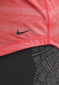 Czerwona sportowa bluzka z poziomymi białymi paskami, z czarnym logo Nike. Zestawiona z czarnymi legginsami z teksturowanymi wzorami.