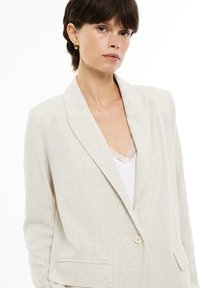 Light beige linen blazer with a single button closure, notch lapels, and two front pockets. Smooth texture with subtle fabric weave.