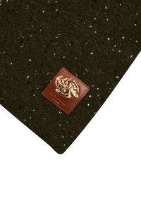 Mørkegrønt tekstureret stof med hvide pletter, med en brun læderpatch præget med et mønster, placeret i hjørnet.