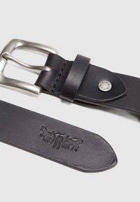 Ceinture en cuir noir avec boucle en métal argenté, ornée d'un motif de cheval embossé sur la lanière et détails de couture le long des bords.