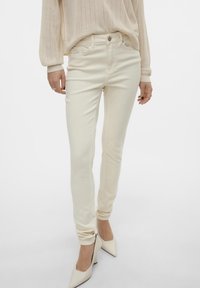 Bílé skinny džíny z denimu s hladkou texturou, designem s pěti kapsami a středním pasem, nosené s lodičkami s špičatou špičkou.