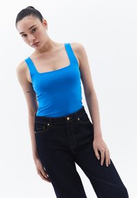 Top ajustado azul con escote cuadrado combinado con jeans oscuros de cintura alta. Textura suave; diseño minimalista sin patrones.