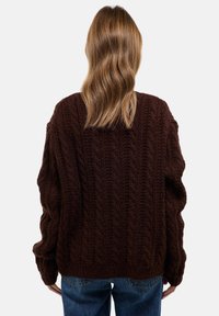 Pull brun en tricot avec un motif torsadé, coupe oversize, manches larges et bord-côtes. Vue de dos, porté sur un jean bleu.