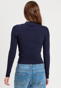 Granatowy sweter z prążkowanej dzianiny z długimi rękawami, okrągłym dekoltem i fakturowanym wzorem. Połączony z jasnoniebieskimi wysokimi jeansami.