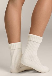 Hvide ribbede sokker med en foldet manchet, der viser en blød tekstur og et subtilt mønster, placeret på en neutral baggrund.