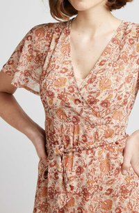 Robe portefeuille florale en tissu pêche doux, avec un décolleté en V profond, des manches courtes et une ceinture à nouer. Le motif comprend des fleurs rouges et orange ainsi que des motifs paisley.