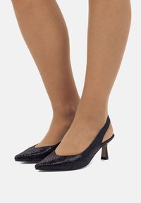 Zapatos de tacón destalonados negros con punta puntiaguda y un patrón de piel de serpiente texturizada, que cuentan con un tacón modesto y un diseño abierto en la parte posterior para facilitar su uso.