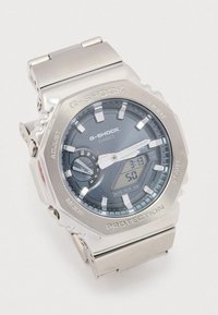 G-Shock horloge met een roestvrijstalen band, groot rond uurwerk, grijze wijzerplaat, zilveren accenten, analoge en digitale weergave, en beschermende bezel.