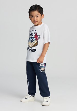 Biały bawełniany t-shirt z grafiką małpy w okularach przeciwsłonecznych, zestawiony z granatowymi spodniami dresowymi z dopasowanym wzorem i elastycznymi mankietami.