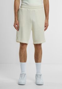 Lys kremfargede strikkede shorts med ribbestruktur, med bred elastisk midje og rullede ermer, kombinert med hvite sneakers og sokker.