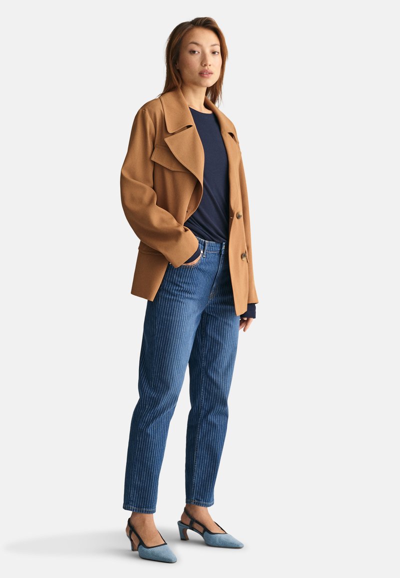 Veste oversized marron avec un col cranté, haut bleu marine, jeans rayés bleus et chaussures à talons compensés bleues. Design structuré.