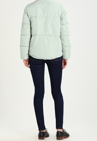 Lys grøn pufferjakke med vandret syninger, en rund krave og en afslappet pasform, parret med mørkeblå skinny jeans og sorte sko.