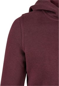 Burgundská mikina s kapucňou, vyrobená z mäkkej, textúrovanej látky, s šnúrkami na kapucni a elegantným dizajnom, pričom má prešité akcenty na pleciach.