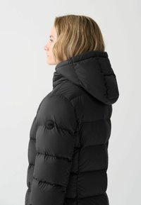 Melnā pūkaina jaka ar kvadrātveida rakstu, izteikts kapuce un logotipa elements uz kreisā piedurknes. Gluda tekstūra un viegls izskats.