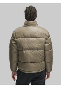 Paks vahe roheline jakk kõrge kaelusega, tikitud tekstuur ja peene logo detail taga. Pikad varrukad ja relax-fit.