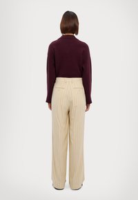 Dunkellila Strickpullover mit lockerer Passform, kombiniert mit hellbeigen, gestreiften Hosen mit hoher Taille und Taschen.