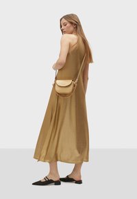 Zlaté saténové maxi šaty s volnějším střihem, nastavitelné ramínka, nošeny s malou zlatou crossbody kabelkou. Černé zdobené muly doplňují outfit.