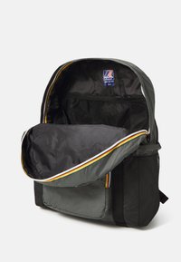 Mochila gris con una gran apertura, bolsillo de malla en el interior, acento de rayas amarillas y rojas, y bolsillos laterales texturizados en negro.