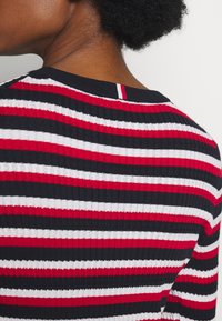 Pull tricoté avec des rayures horizontales noires, rouges et blanches. Tissu côtelé texturé avec un col rond et un détail au dos.