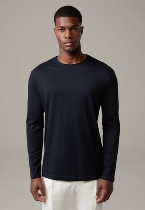 Black long-sleeve t-shirt made of stretchy material with a round neckline and fitted sleeves, paired with light-colored pants.
