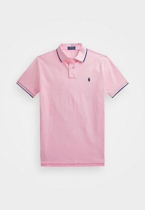 Jasnoróżowa koszulka polo z krótkim rękawem, z granatowym wykończeniem kołnierzyka i mankietów, z pliską na dwa guziki oraz małym granatowym haftowanym logo na piersi.