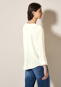 Hvid struktureret bluse med trekvartærmer, rund halsudskæring og en afslappet pasform, parret med blå jeans.