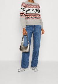 Szary sweter dzianinowy z reniferami i wzorami geometrycznymi, niebieskie szerokie dżinsy, srebrna metaliczna torebka oraz sportowe srebrne trampki.