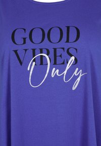 T-shirt in cotone viola con grande scritta nera che recita "GOOD VIBES" e una scrittura corsiva bianca per la parola "Only". Design semplice.