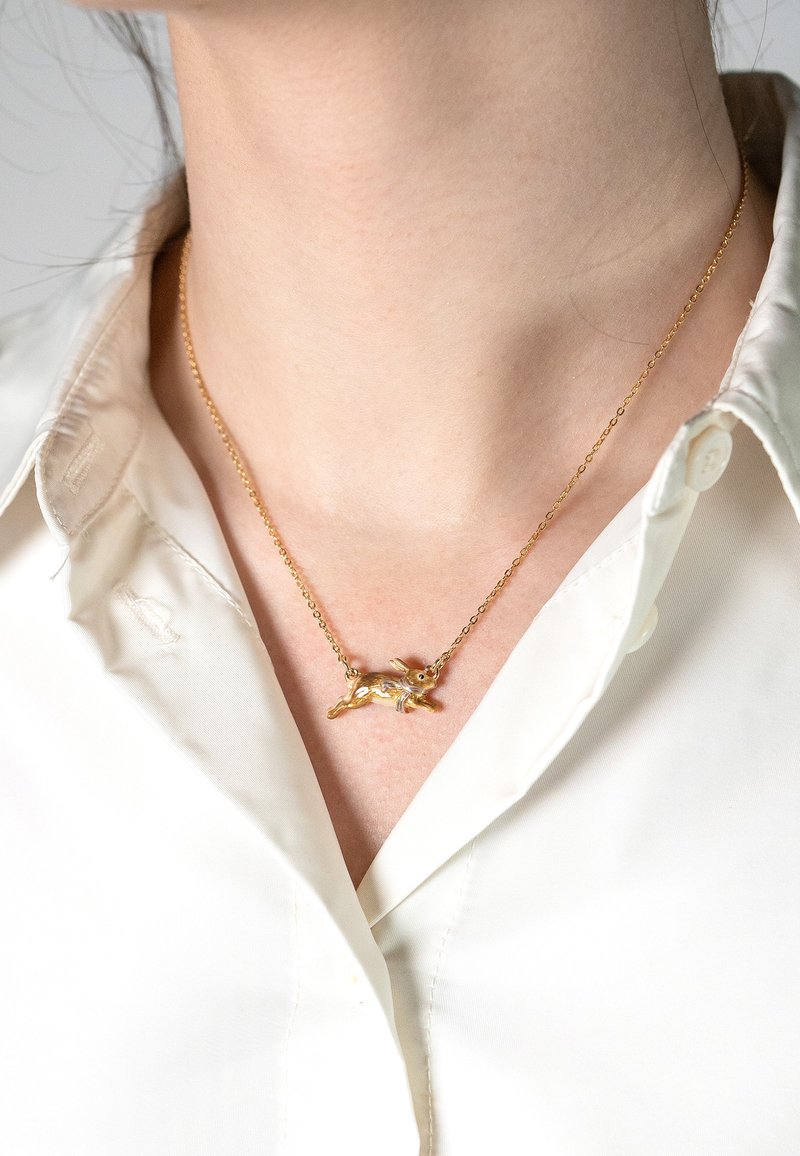 Gold-tone necklace featuring a detailed rabbit pendant on a fine chain, worn over a white button-up shirt.