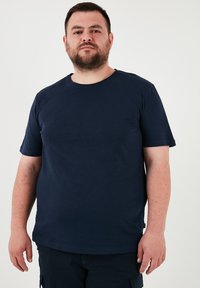 Tricou bleumarin cu mânecă scurtă, cu guler rotund și textură netedă, având un croi lejer și un detaliu subtil de etichetă pe lateral.