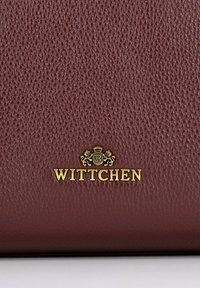 Bordowy, teksturowany portfel ze skóry z złotym, wytłoczonym logo "WITTCHEN" oraz misternym wzorem herbu na środku.