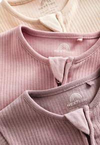 Three baby tops in varying shades of pink, featuring a ribbed texture and rounded collars, with button closures and brand labels visible.
