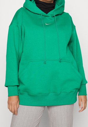 Osoba nosící jasně zelenou mikinu Nike s kapsou vpředu a stahovacími šňůrkami, doplněnou světle šedými pruhovanými kalhotami.