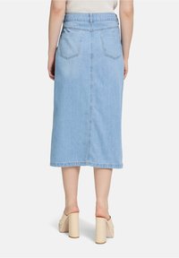 Lichtblauwe denim midi-rok met een knoopsluiting, achterzakken en stikdetails. Model draagt beige hakken.