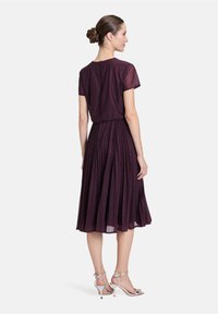 Une robe plissée violette avec des manches courtes, une taille cintrée et une fermeture à l'arrière en forme de clé. Associée à des sandales à talons hauts argentées avec des lanières.