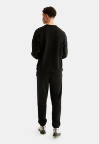 Black sweatshirt with a crew neck and ribbed cuffs, paired with matching tapered joggers. The fabric appears soft with a smooth texture.
