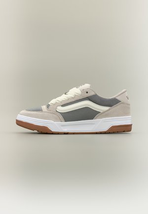 Low-top sneaker with beige suede, gray mesh panels, white side stripe, white laces, and gum rubber sole on neutral background.