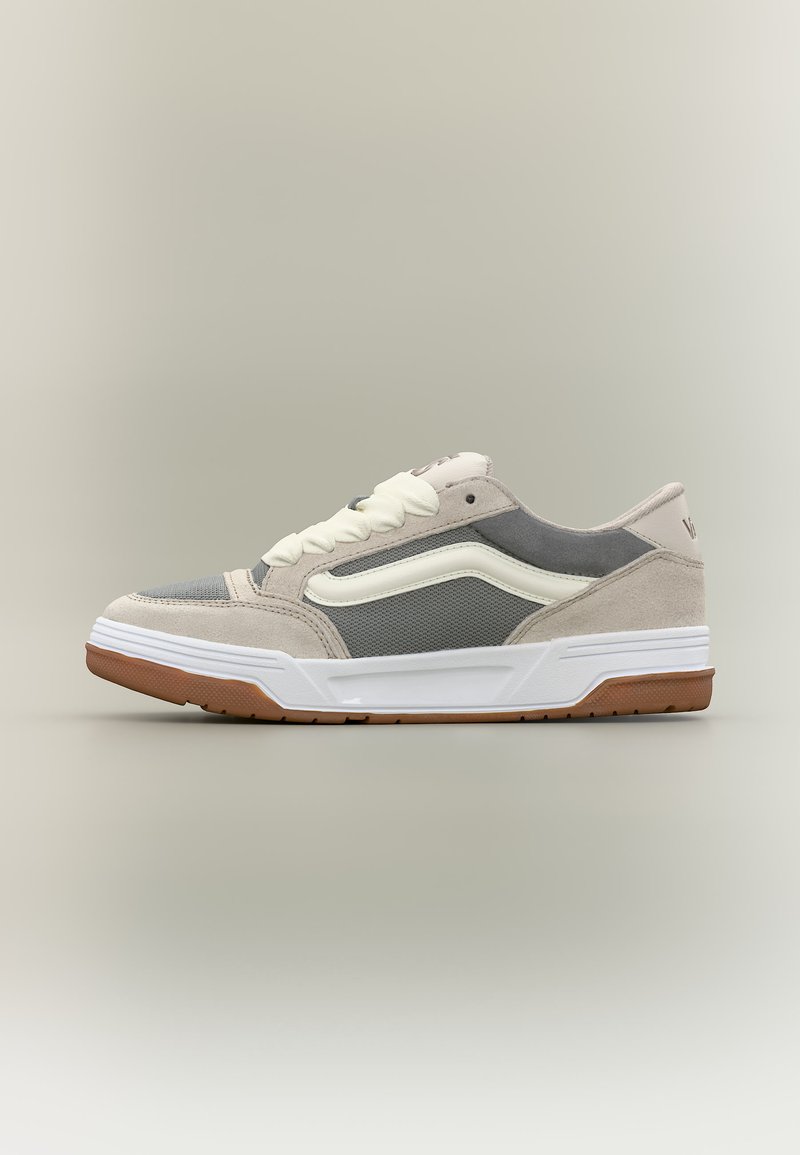 Αθλητικό παπούτσι χαμηλού ύψους με μπεζ σουέντ, γκρι πλέγμα σε πάνελ, λευκή πλαϊνή ρίγα, λευκά κορδόνια και σόλα από καουτσούκ χρώματος καραμέλας σε ουδέτερο φόντο.
