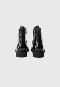 Botas de tobillo de cuero negro con un acabado brillante, detalle de cremallera en la parte posterior y suela gruesa. Diseñadas para la durabilidad y la comodidad.