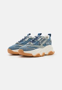Blue denim sneakers with a textured upper, thick white midsole, and gum rubber outsole. Features frayed details and blue laces.