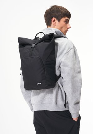 Black roll-top backpack with adjustable straps, front pocket, and a smooth texture. Minimalist design with branded logo at the bottom.