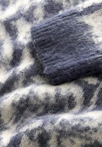 Hellcreme und dunkelgrauer gestrickter Pullover mit einer weichen, flauschigen Textur und gerippten Bündchen, der eine Farbmischung in einem melierten Muster zeigt.