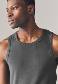 Débardeur gris côtelé avec un col rond et de larges emmanchures. Présente une coupe près du corps, une texture douce et des coutures nettes aux bords.