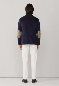 Chaqueta navy con parches en los codos en beige, combinada con pantalones blancos. Diseño sencillo, corte recto y textura suave.