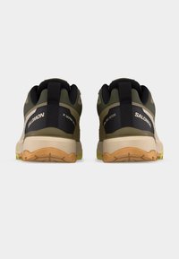 Ζευγάρι παπουτσιών για trail running Salomon σε ελιά πράσινο και μπεζ, εμφανιζόμενα από πίσω, με μαύρες ταμπέλες στη φτέρνα και πορτοκαλί υφασμένα πέλματα.