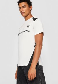 Short-sleeve white athletic shirt featuring a black logo and side accents, made of breathable fabric with a fitted design.