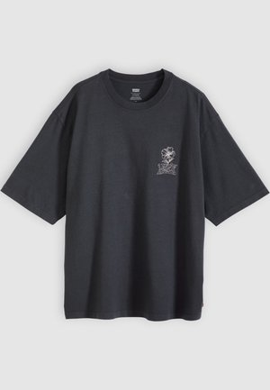 T-shirt noir oversize à manches courtes, col rond, avec un petit motif de fleur blanche et du texte sur le côté gauche de la poitrine.