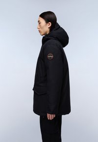 Černá voděodolná bunda s kapucí, texturovaná tkanina, boční kapsy a kruhová nášivka s logem na levém rameni.