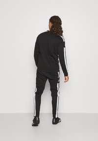 Survêtement de sport noir avec des rayures blanches sur les manches et les côtés, fabriqué en tissu doux ; design ajusté, incluant un pantalon de jogging et un sweat-shirt.
