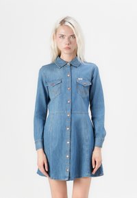 Denim dress with a collar, long sleeves, and button front. Features two chest pockets with contrasting stitching and a flared hem. Light blue color.